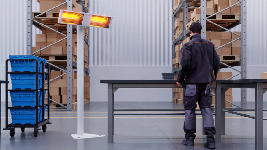 Two infrared heaters on a stand, warming a working in a warehouse